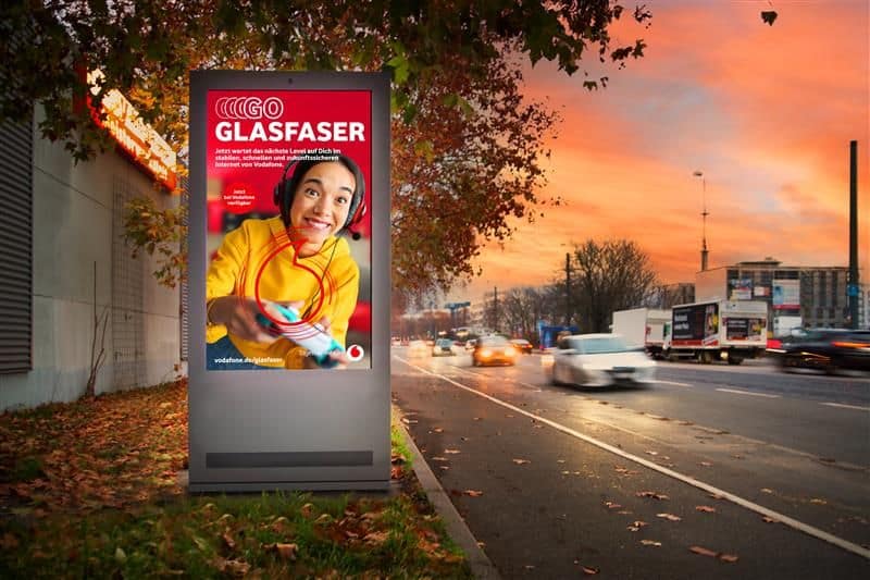 Digitales CityLightPoster neben einer Hauptverkehrsstraße bei Dämmerung