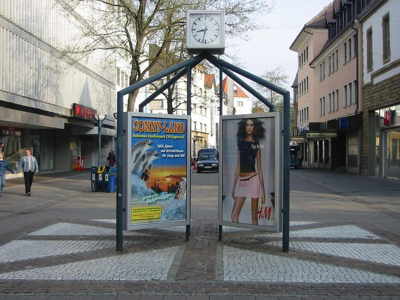 CityLightPoster mit einer Stadtuhr in einer Fußgängerzone CityLightPoster mit einer Stadtuhr in einer Fußgängerzone
