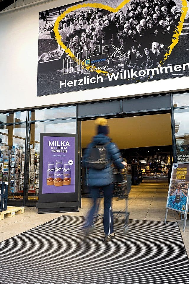 Digitales City-Light-Poster vor dem Eingang zu einem Edeka-Markt Digitales City-Light-Poster vor dem Eingang zu einem Edeka-Markt